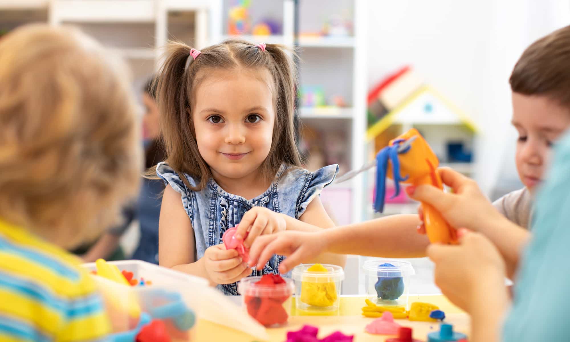 Young children doing hands-on sensory and fine-motor play with coloured modelling dough at a table